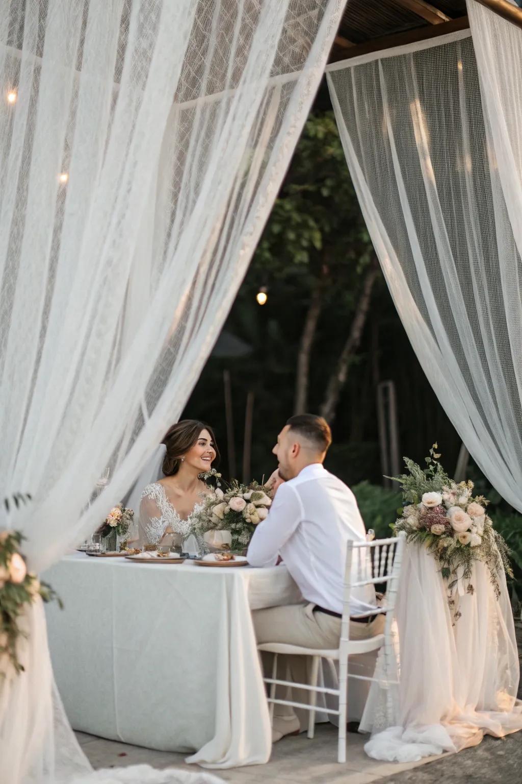 A bride and groom table surrounded by sheer hanging fabrics for an ethereal effect.