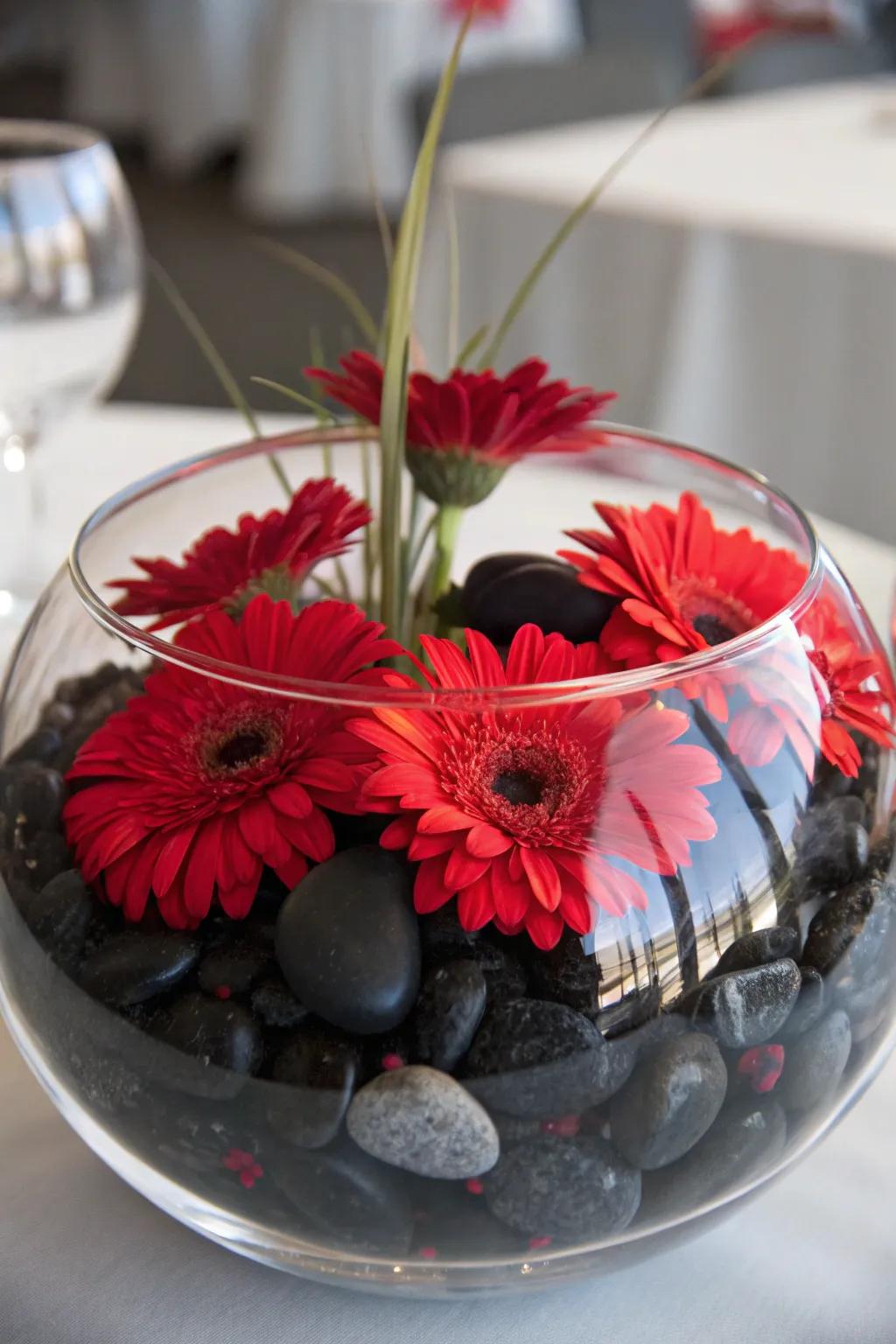 Scarlet blossoms floating gracefully over dark stones encapsulated in a clear glass bowl, forming a tranquil centerpiece.